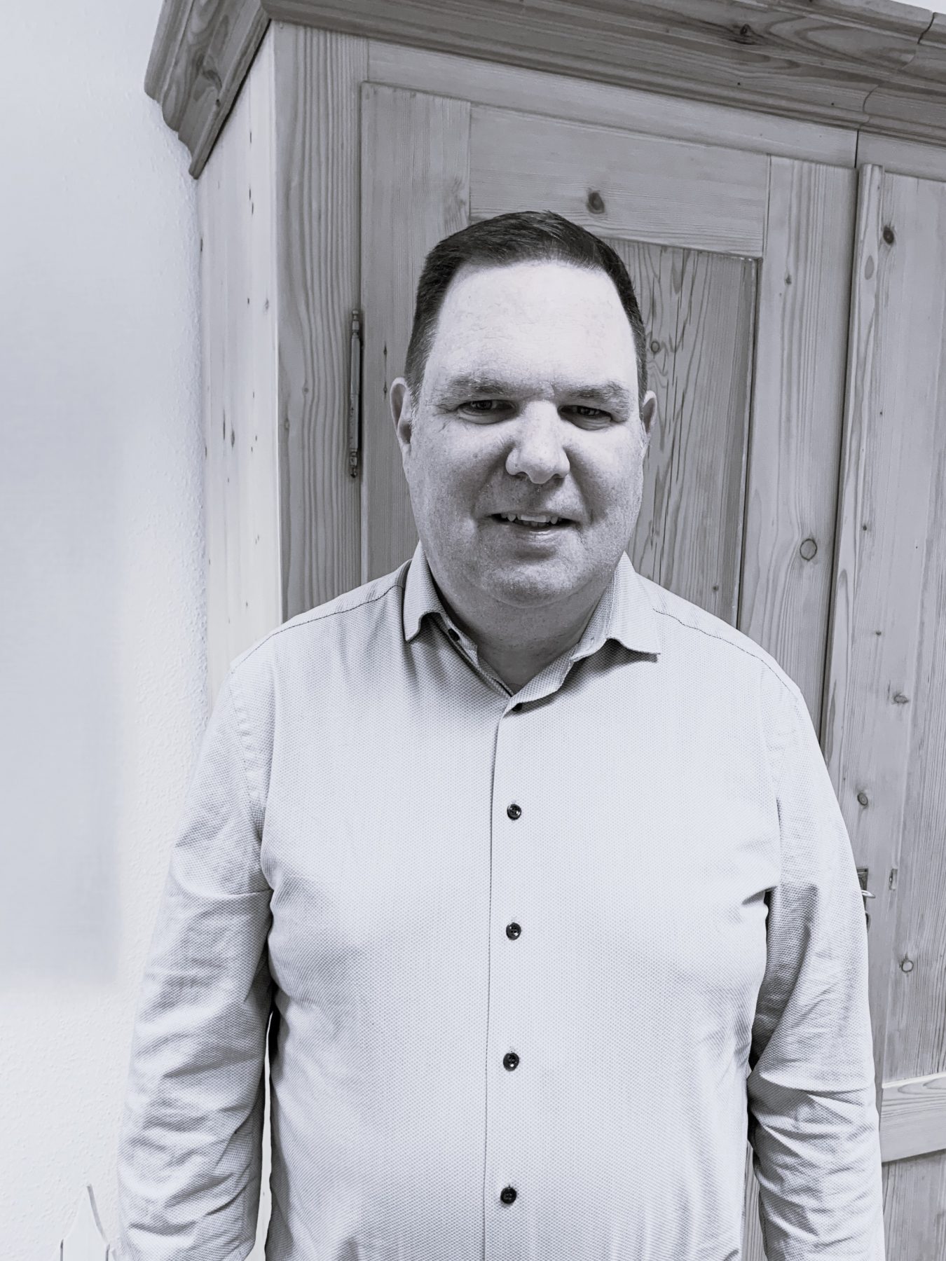 Mann mit kurzen Haaren und hellem Hemd vor Kasten stehend